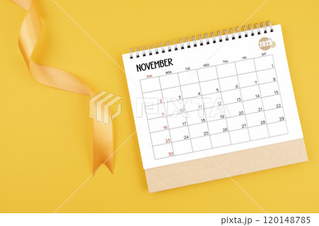 November 2025 desk calendar with yellow ribbon on yellow background. 120148785