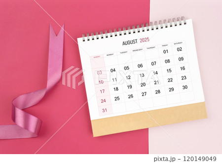 August 2025 desk calendar and pink ribbon on pink background. August 2025 desk calendar and pink ribbon on pink background. 120149049