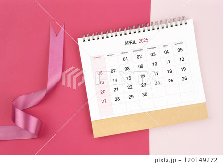 April 2025 desk calendar and pink ribbon on pink background. 120149272