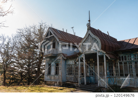 Abandoned vintage house with intricate architecture under a clear sky surrounded by trees in the afternoon light 120149676