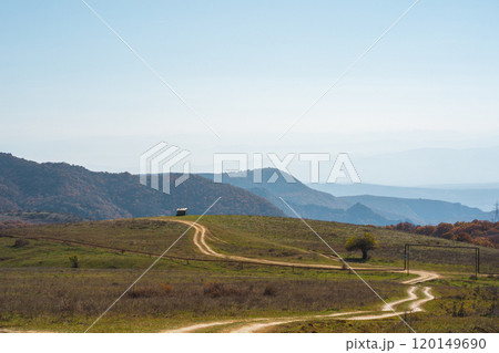 Serene winding dirt road through green hills under a clear blue sky in a tranquil countryside setting Serene winding dirt road through green hills under a clear blue sky in a tranquil countryside setting 120149690