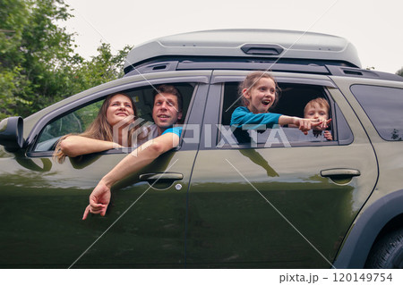 A cheerful family is enjoying a funfilled road trip, sharing laughter and excitement as they travel in a green SUV A cheerful family is enjoying a funfilled road trip, sharing laughter and excitement as they travel in a green SUV 120149754
