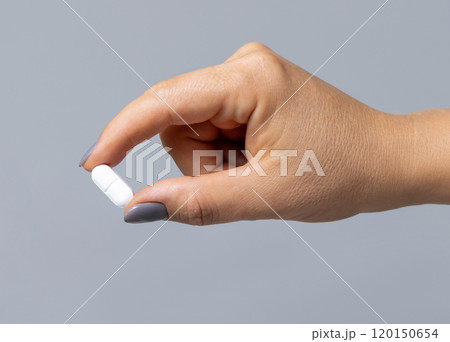 Female hand holding a white pill with fingers closeup against grey, Healthcare concept Female hand holding a white pill with fingers closeup against grey, Healthcare concept 120150654