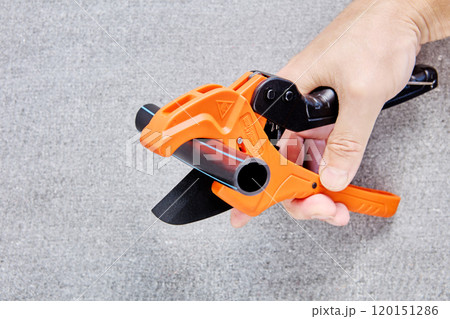 Cutter scissors for plastic pipes are equipped with ratchet mechanism, hand holds plumber tool on background of flat slate. 120151286