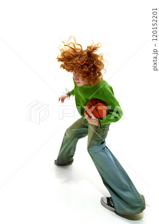 Energetic young man with curly hair in green sweater runs with basketball, hair in motion against white studio background. 120152201