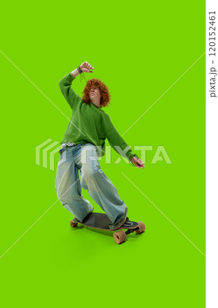 Dressed stylish old-school outfit young man riding on skateboard with happiness and joy against vibrant green studio background. 120152461