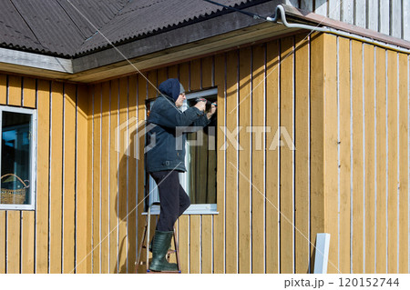 Installing metal window slopes and metal window sills in window opening from facade side, roofing contractor works standing on steel folding ladder. 120152744