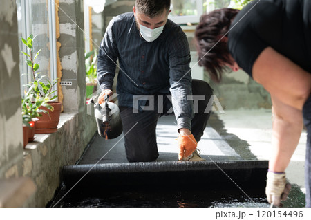 A man and a woman are engaged in waterproofing the floor in the house. 120154496