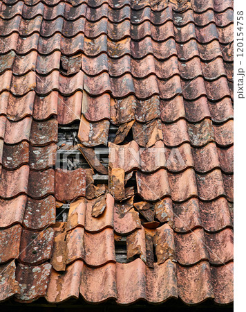 Damage to the clay tile roof of a historic house with some roof tiles missing, broken roof tiles Damage to the clay tile roof of a historic house with some roof tiles missing, broken roof tiles 120154758