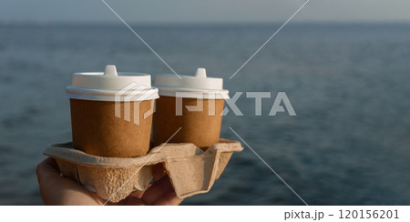 banner two brown cup of drink in woman's hand on Baltic Sea coast, close up, copy space 120156201