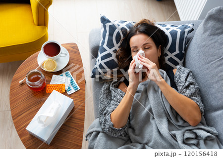 Woman is laying on a couch with a tissue 120156418
