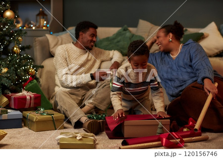 Full length portrait of modern African American family celebrating Christmas together in cozy home with focus on little boy opening presents copy space Full length portrait of modern African American family celebrating Christmas together in cozy home with focus on little boy opening presents copy space 120156746