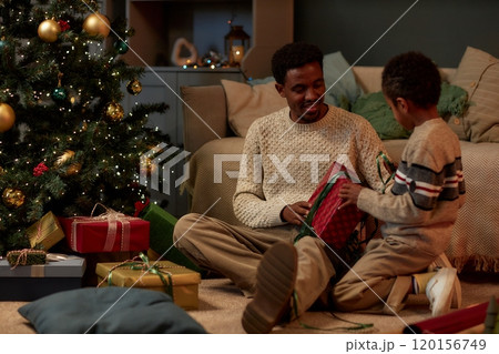 Full length portrait of happy African American family of caring father and son opening Christmas presents together sitting on floor 120156749