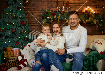 Happy family hugging warmly next to Christmas tree and smiling cheerfully on Christmas Eve in a Happy family hugging warmly next to Christmas tree and smiling cheerfully on Christmas Eve in a 120156771