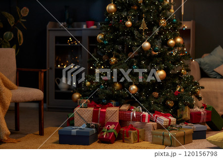 Background image of beautiful Christmas tree with gold accents and pile of presents in cozy home interior in low lighting copy space 120156798