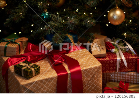 Closeup background image of big gift box with red bow piled under Christmas tree in dim lighting Closeup background image of big gift box with red bow piled under Christmas tree in dim lighting 120156805