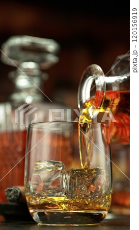 Pouring whiskey into glass full of ice cubes. Pouring whiskey into glass full of ice cubes. 120156919
