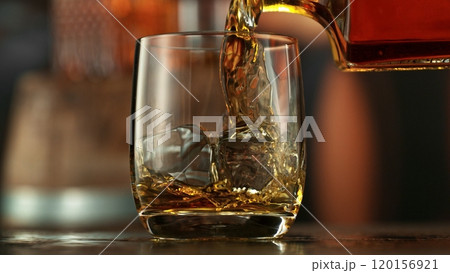Pouring whiskey into glass full of ice cubes. Pouring whiskey into glass full of ice cubes. 120156921