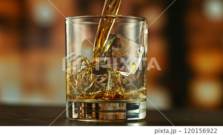 Pouring whiskey into glass full of ice cubes. Pouring whiskey into glass full of ice cubes. 120156922