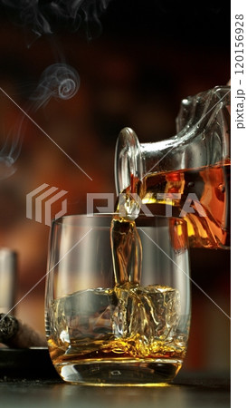 Pouring whiskey into glass full of ice cubes. 120156928