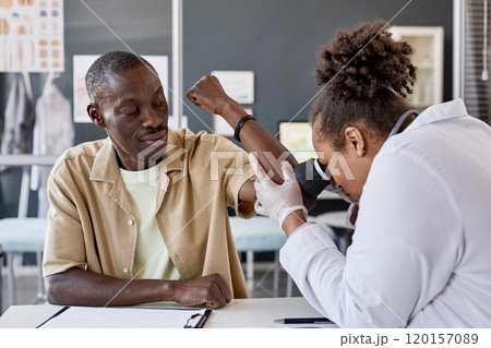 Portrait of smiling adult African American man visiting doctor with dermatologist examining skin using dermascope in clinic 120157089