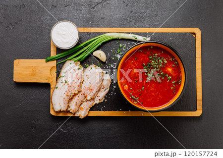 Traditional borscht soup with sour cream, green onions, garlic, and pork slices served on board 120157724