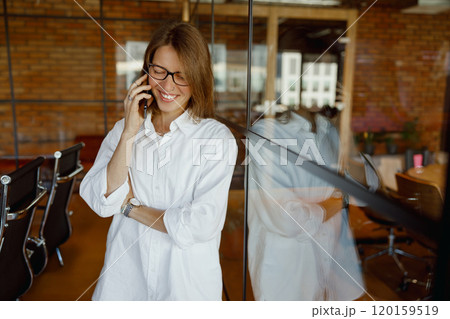 A Smiling Woman Engaged in a Phone Conversation in a Modern Office Environment full of Life 120159519