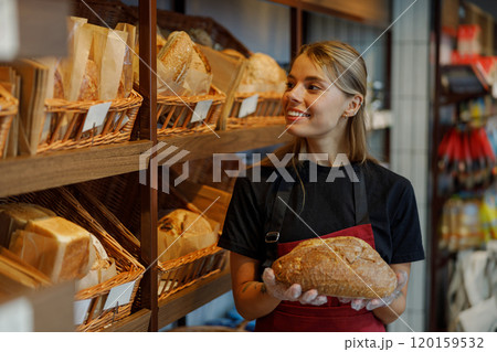 A young baker proudly holding a freshly baked loaf of bread in a charming artisan bakery 120159532