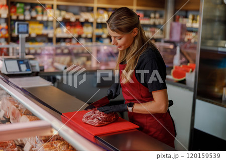 A woman is skillfully preparing fresh meat at a busy market counter for eager shoppers to see A woman is skillfully preparing fresh meat at a busy market counter for eager shoppers to see 120159539