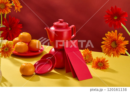 A teapot on a sphere is surrounded by dishes, lucky envelopes, tangerines, and Gerbera flowers on a yellow table against a red background in the high-angle template photo with the Tet theme. 120161138