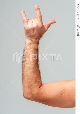 A person makes a hand gesture with the pinky and index finger raised against a plain background 120162995