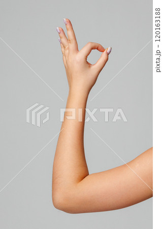 A hand gesturing the OK sign against a simple grey background 120163188