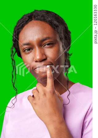 Young woman with curly hair shows a skeptical expression against a bright green background 120163330
