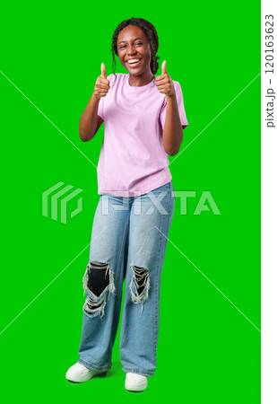 A young woman gives a cheerful thumbs up while wearing a pink shirt and blue jeans against a vibrant green background A young woman gives a cheerful thumbs up while wearing a pink shirt and blue jeans against a vibrant green background 120163623