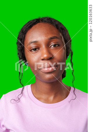 Young woman with an expression of contemplation poses against a bright green background 120163633