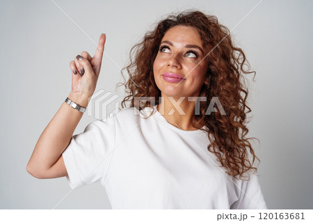 Woman with curly hair thoughtfully pondering in a neutral setting Woman with curly hair thoughtfully pondering in a neutral setting 120163681