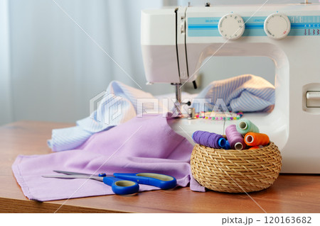 Sewing machine in use on a wooden table, stitching a light fabric in a well-lit indoor workspace 120163682