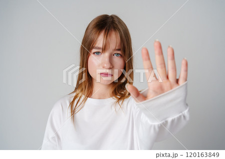 Young woman with long hair holding up her hand against a plain background Young woman with long hair holding up her hand against a plain background 120163849