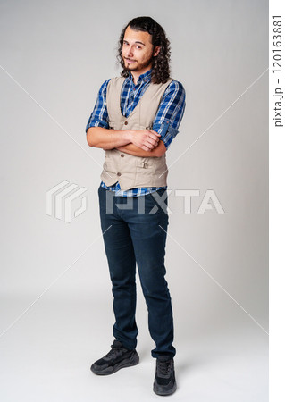A confident young man with curly hair poses against a neutral backdrop 120163881
