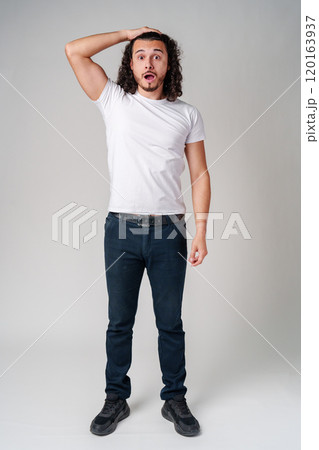 A man with curly hair expresses surprise while looking upwards in a neutral background A man with curly hair expresses surprise while looking upwards in a neutral background 120163937