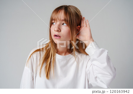 Teen girl with straight hair demonstrates listening pose against a plain background 120163942