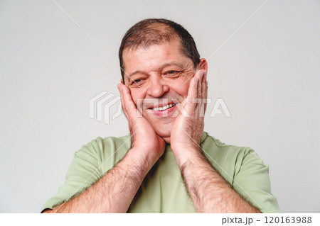Happy middle-aged man showing joy while touching his face against a neutral background Happy middle-aged man showing joy while touching his face against a neutral background 120163988