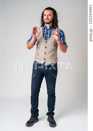 A young man with curly hair dressed in a vest and plaid shirt shows determination while making a fist indoors A young man with curly hair dressed in a vest and plaid shirt shows determination while making a fist indoors 120164061