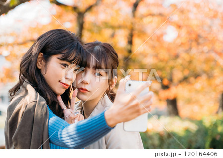 紅葉を背景にスマホで写真を撮る女性二人 120164406
