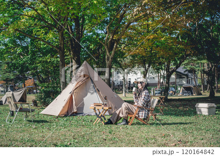 キャンプで椅子に座ってくつろぐ若い女性 120164842