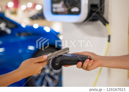 Person makes a contactless payment at a terminal near a charging station with a mobile device. 120167021