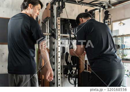 パーソナルジムで会員にトレーニングの見本を見せるトレーナーの男性（腕トレ） 120168556