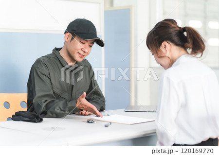 自動車整備工場の受付で説明・見積もり・提案をする整備士の男性と顧客の女性 120169770