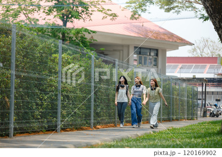Three women walking down a sidewalk in front of a building 120169902