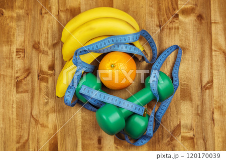 Two dumbbells, a centimeter, bananas and an orange lie on a wooden surface Two dumbbells, a centimeter, bananas and an orange lie on a wooden surface 120170039
